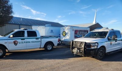 Two U.S. Park Ranger pickup trucks are parked on pavement. Emergency service trailers can be seen in the background. NPS Photo/L. Stoops