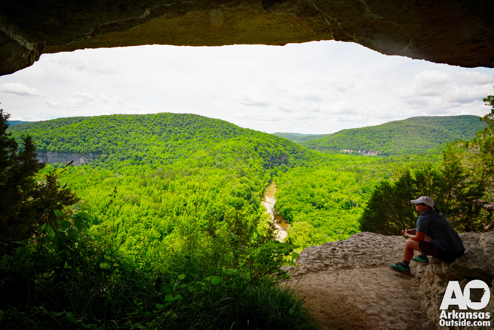 A hiker enjoying the view of the Buffalo National River from the shade of an overhang on a bluff line.