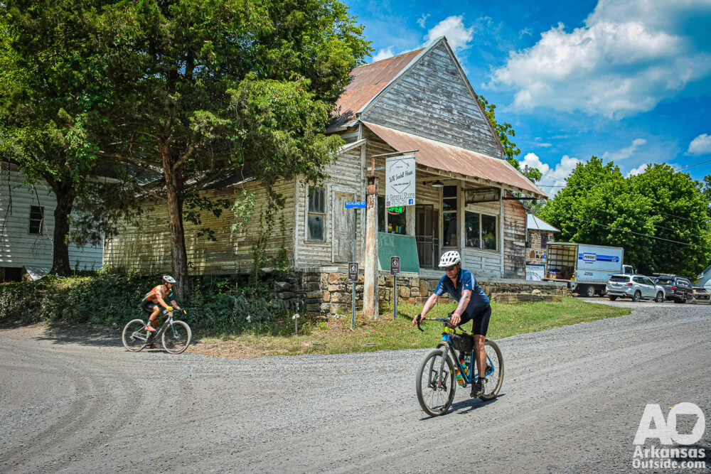 Cyclists riding gravel roads past an old general store.