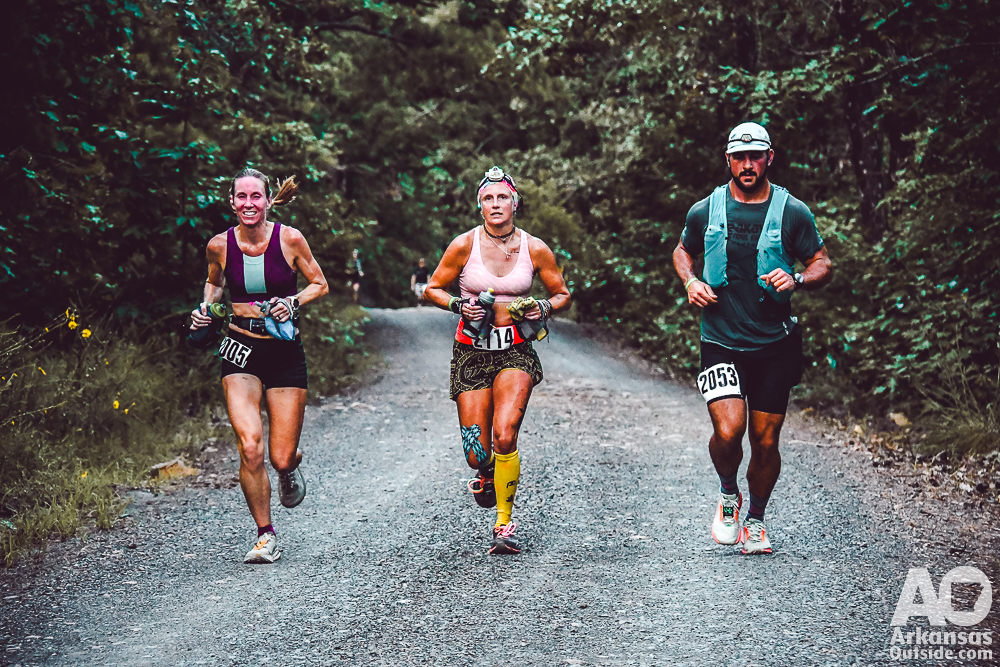 Three runners running abreast on a gravel road.