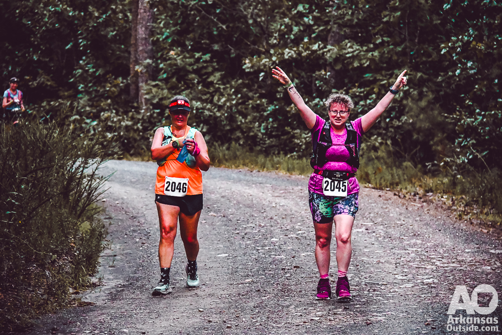 Two women walking on a gravel road.