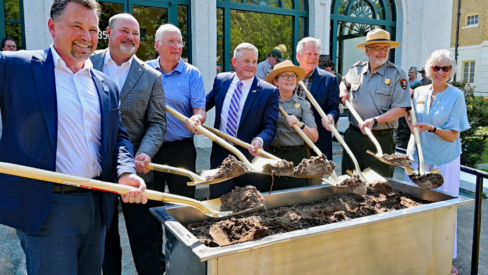 Several digitaties using shovels to turn dirt in a bin.