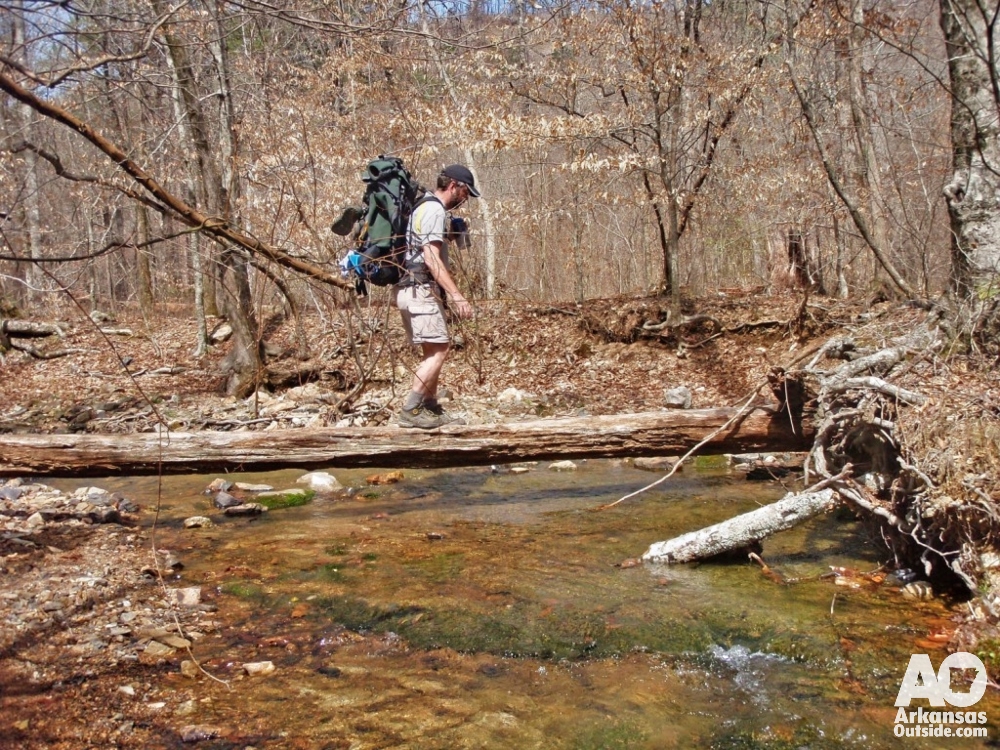 Hiker crossing the Little Missouri River on a log on the Eagle Rock Loop trail